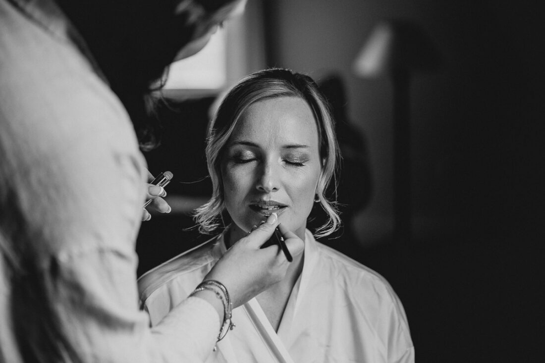Braut beim Getting Ready auf der Maisenburg, während ihr Lippenstift aufgetragen wird. Schwarz-Weiß-Fotografie von Patricia Hamann, Hochzeitsfotografin Ulm.