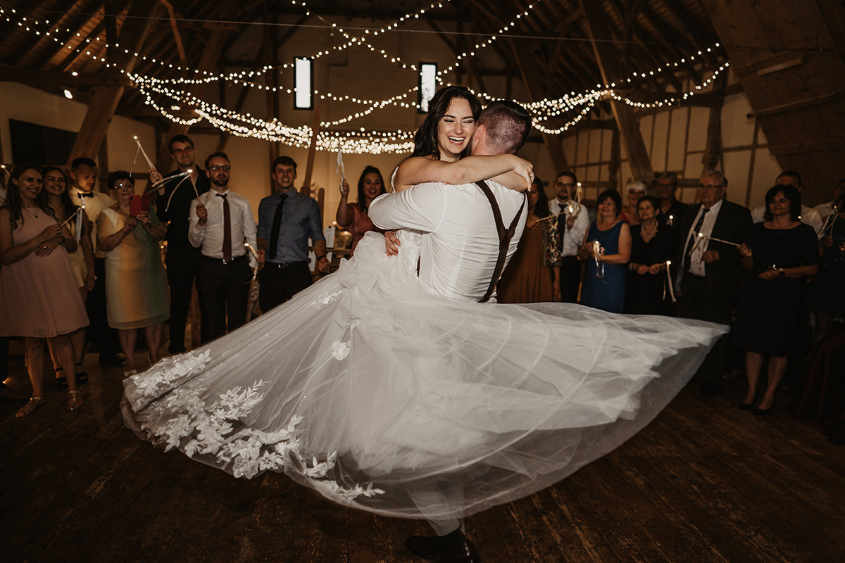 Brautpaar tanzt ausgelassen bei Hochzeit in Ulm. Bräutigam hebt die Braut hoch, umgeben von Gästen.