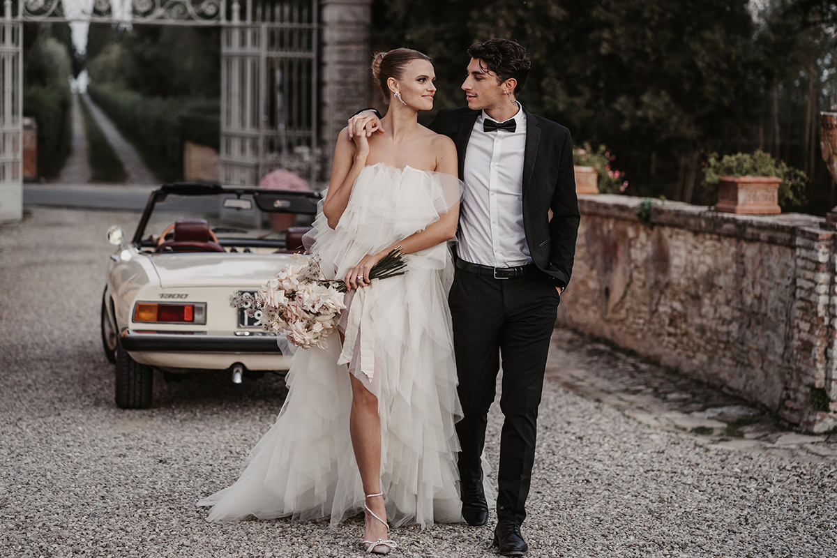 Bei ihrer Hochzeit in der Toskana läuft das Brautpaar eng zusammen von ihrem Brautauto weg und schaut sich verliebt an.