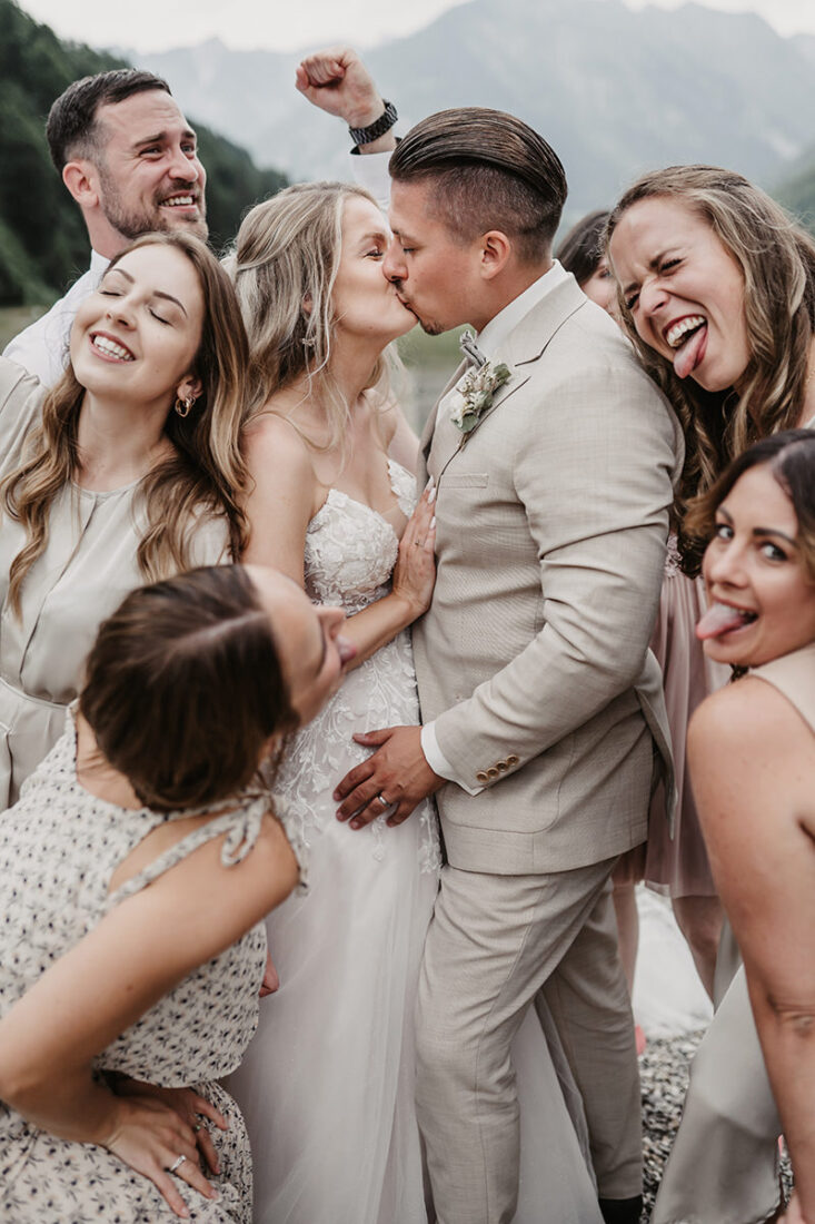 Hochzeitsfotograf Patricia Hamann fotografiert küssendes Brautpaar inmitten ihrer jubelnden Freunde.