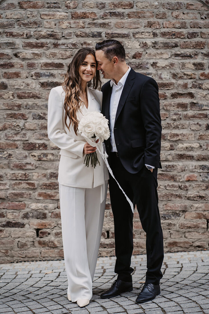 Brautpaar steht vor einer Steinmauer und schaut verliebt in die Kamera - fotografiert von Patricia Hamann