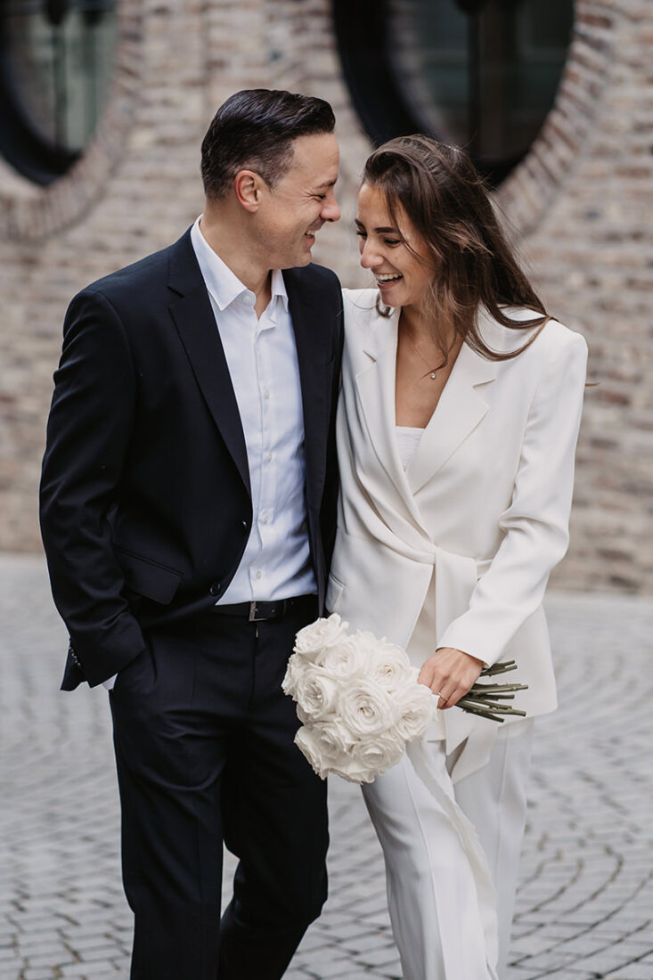 Brautpaar läuft durch Stadt und sieht sich lachend an.