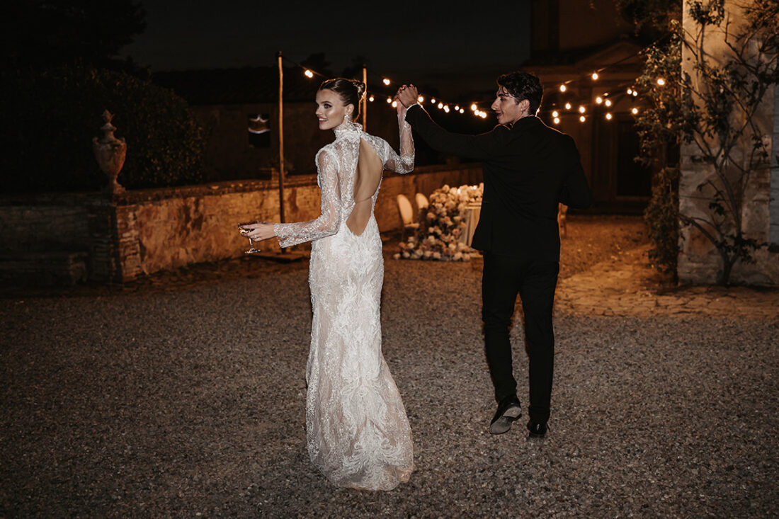 Von hinten fotografiertes Brautpaar läuft zum Brauttisch und dreht sich zu ihren Gästen um und hält die Hände jubelnd in die Höhe - Hochzeitsfotograf Patricia Hamann