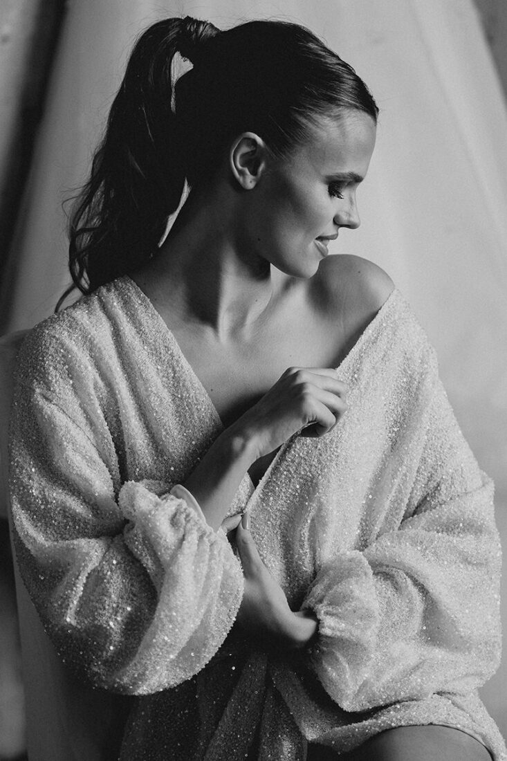 Sitzende Braut zieht sich beim Getting Ready den glitzernen Morgenmantel über die Schulter - Hochzeitsfotograf Patricia Hamann