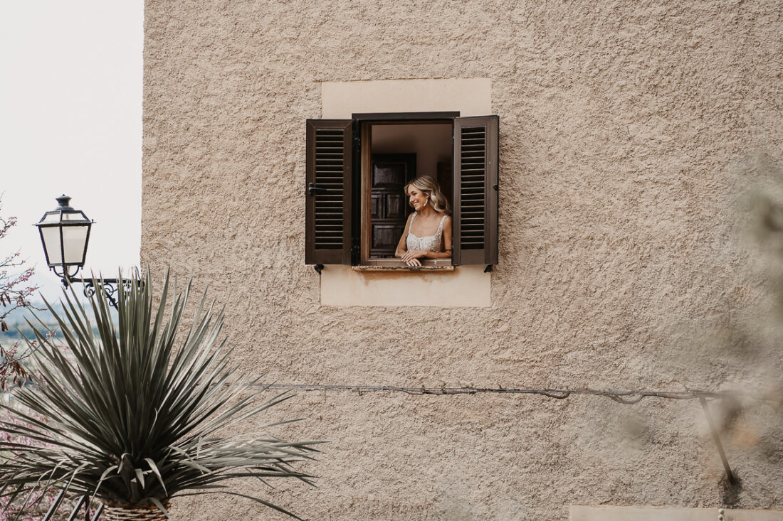Braut schaut verliebt aus dem Fenster einer mallorquinischen Finca - Hochzeitsfotograf Patricia Hamann