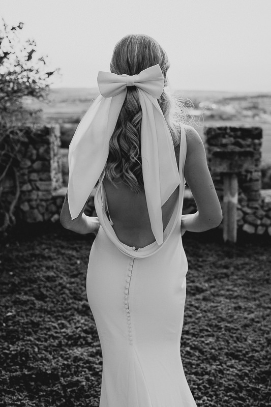 Rückenansicht einer Braut im Brautkleid mit einer Schleife im Haar.