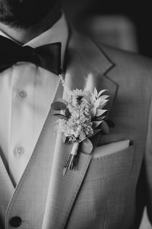 Detailaufnahme eines Hochzeitsanzugs mit Fliege und Boutonniere aus hellen Blüten. Schwarz-Weiß-Fotografie von Patricia Hamann, Hochzeitsfotografin Maisenburg Ulm.
