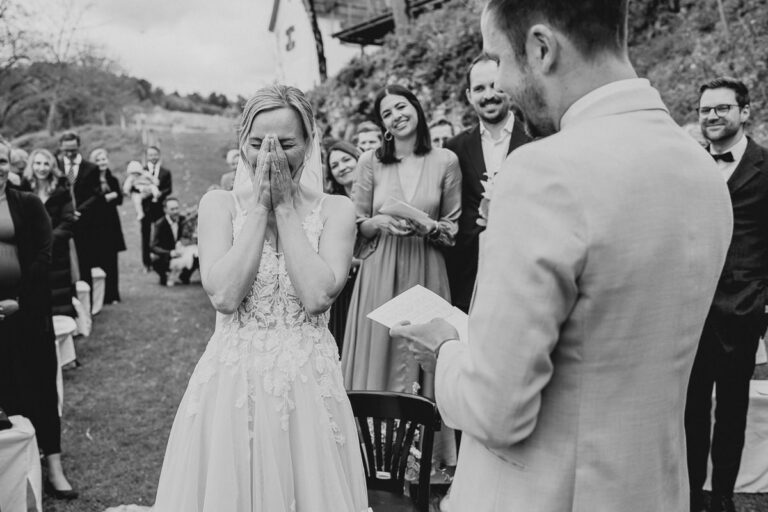 Die Braut hält sich vor Freude die Hände vors Gesicht, während der Bräutigam auf der Maisenburg seine persönlichen Eheversprechen vorliest. Foto von Patricia Hamann, Hochzeitsfotografin aus Ulm.