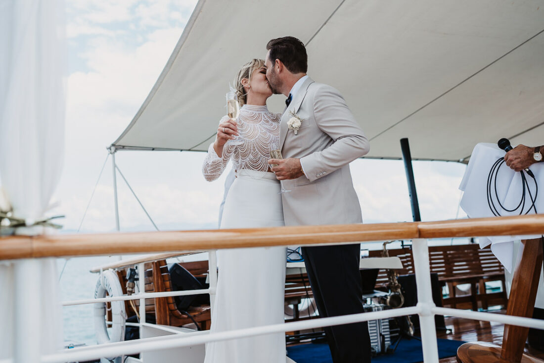 Braut und Bräutigam küssen sich beim Anstoßen mit Sektgläsern auf dem Deck der Hohentwiel während ihrer Hochzeit auf dem Bodensee, fotografiert von Patricia Hamann, Hochzeitsfotograf Werft1919
