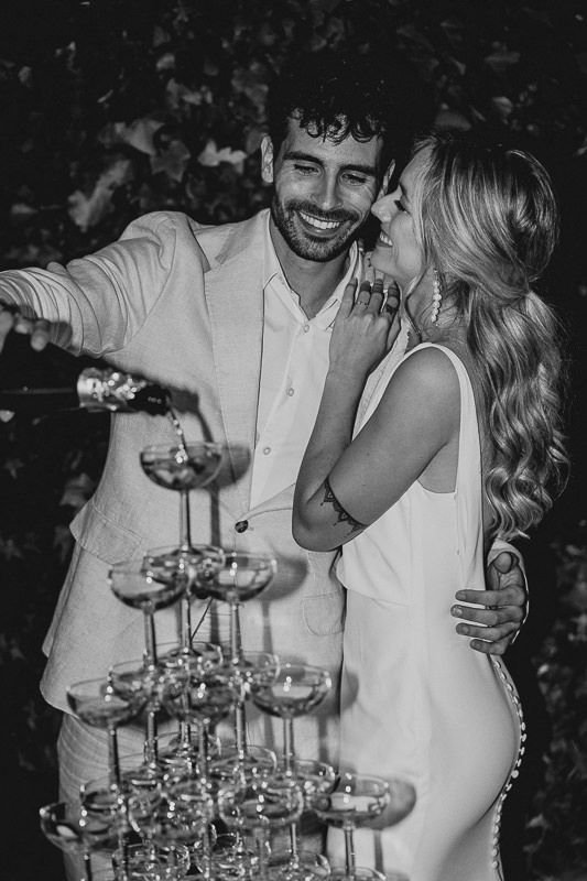 Frisch vermähltes Paar gießt gemeinsam Champagner in eine Glaspyramide während ihrer Hochzeit auf Mallorca.