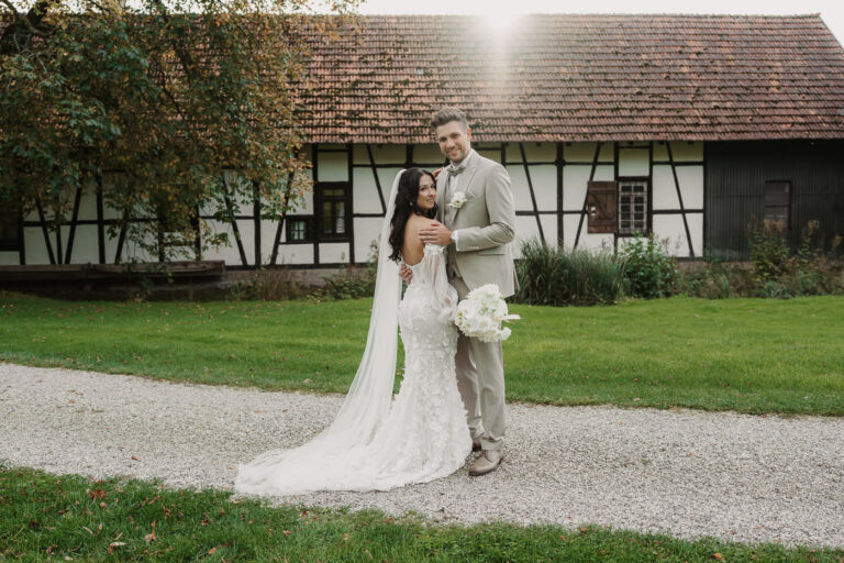 Brautpaar schaut in die Kamera vor der Kulisse des Steinbachhofes im warmen Sonnenlicht.