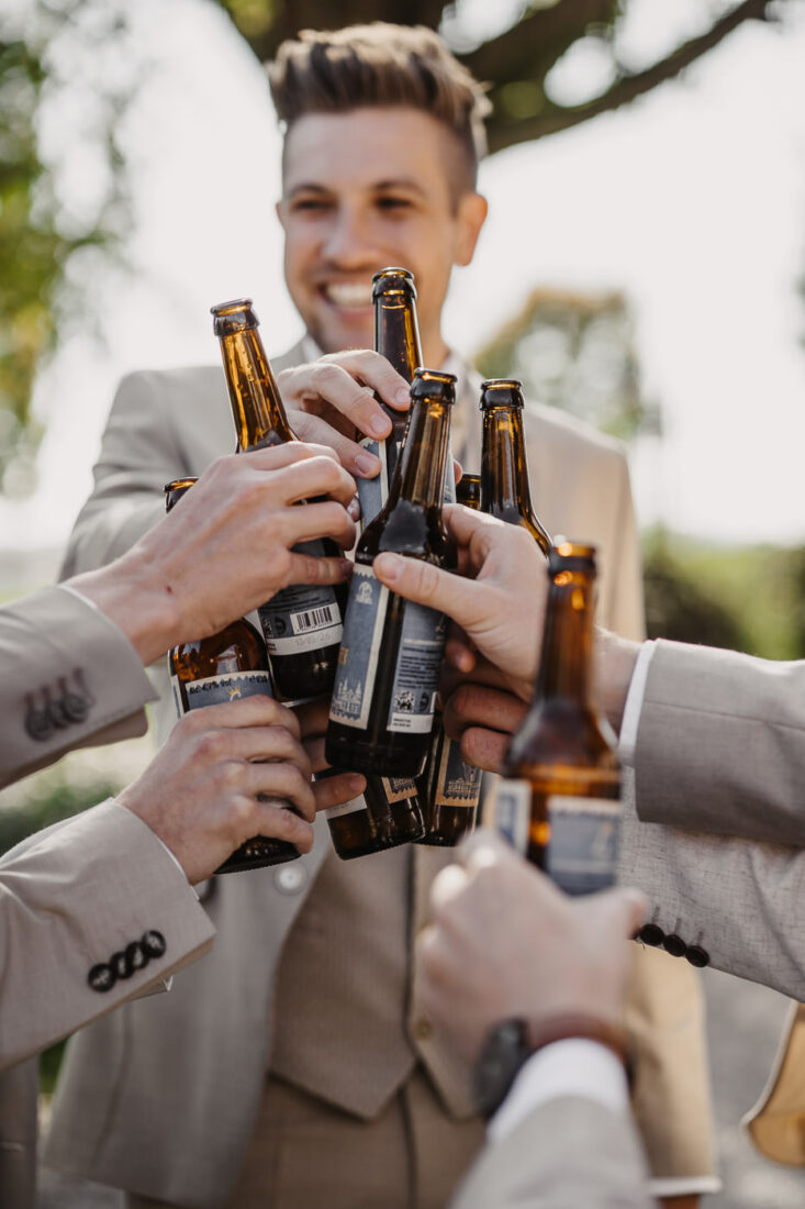 Der Bräutigam und seine Trauzeugen stoßen mit Bierflaschen an.
