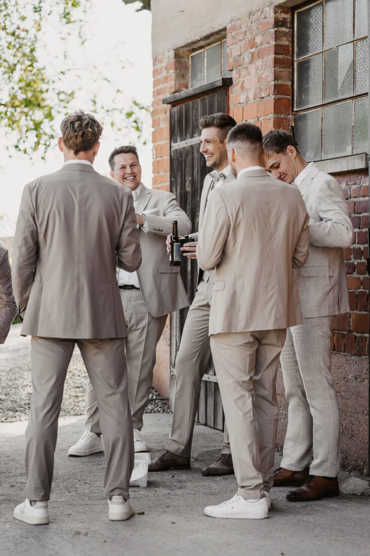 Der Bräutigam steht mit seinen Freunden vor einem Gebäude auf dem Steinbachhof und lacht