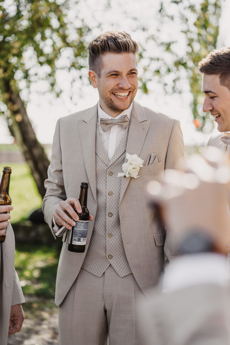 Der Bräutigam lacht entspannt während des Anstoßens mit seinen Trauzeugen.
