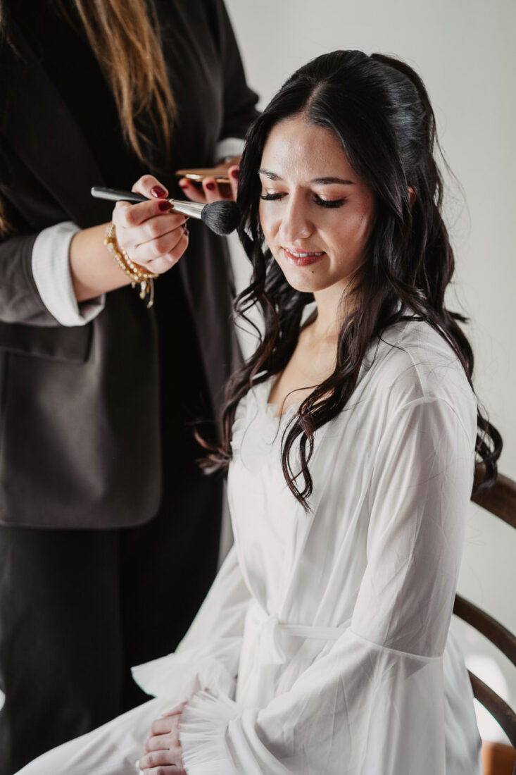Detailaufnahme der Braut, wie sie gerade von ihrer Stylistin geschminkt wird.