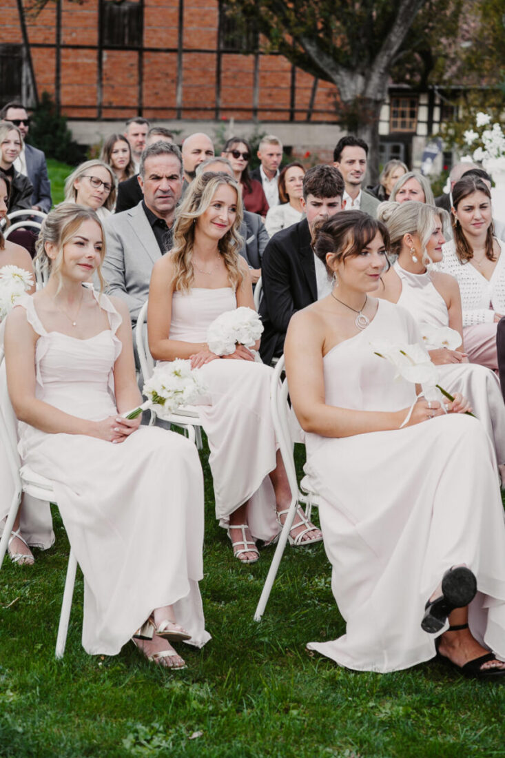 Drei Brautjungfern in pastellfarbenen Kleidern halten Blumensträuße während der Trauung bei Ludwigsburg.