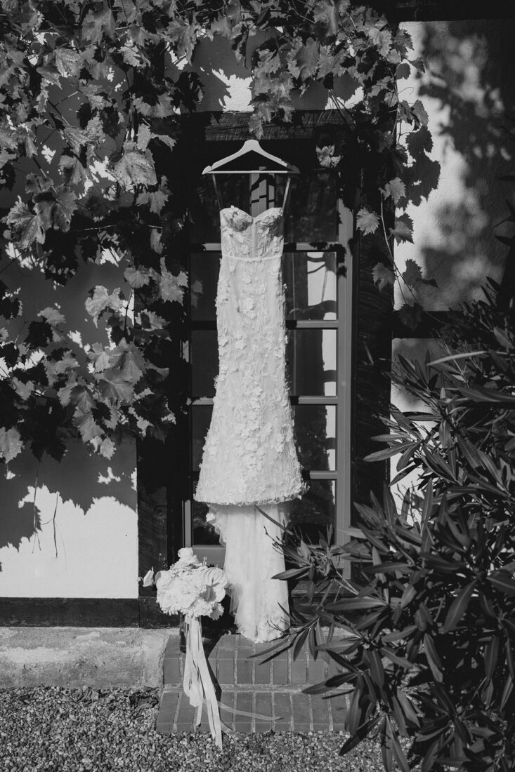 Das Brautkleid hängt an einem historischen Fenster des Steinbachhofs, umrahmt von Weinreben.