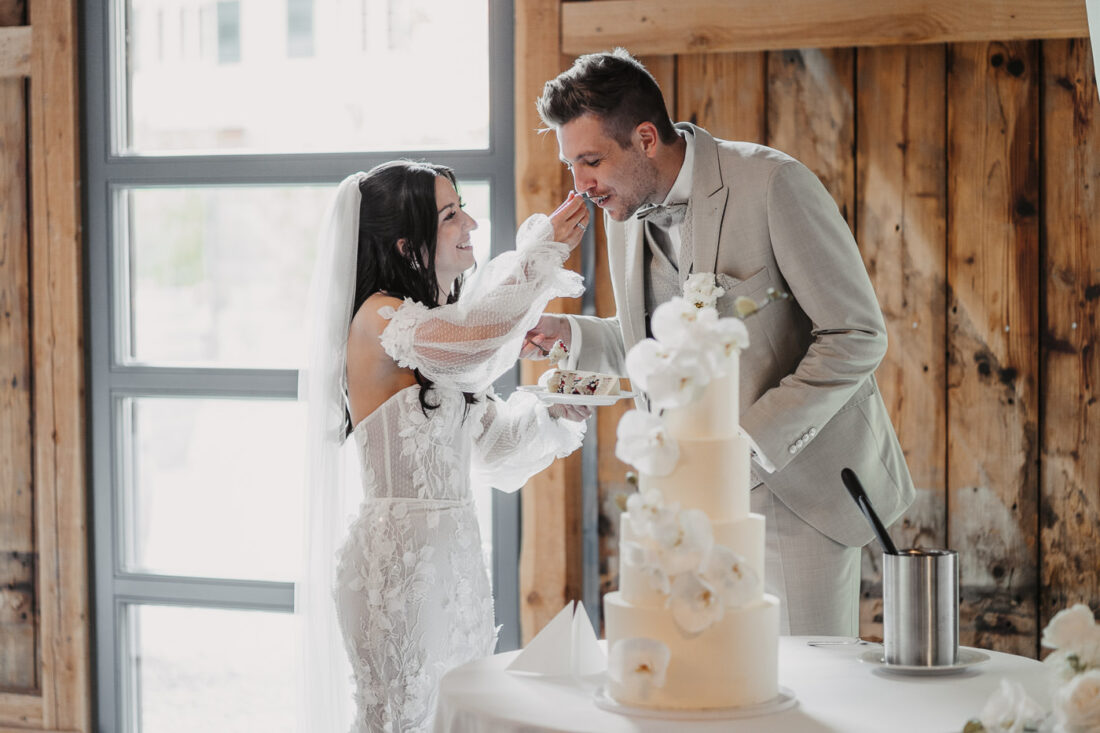 Die Braut füttert den Bräutigam spielerisch mit dem ersten Stück der Hochzeitstorte.