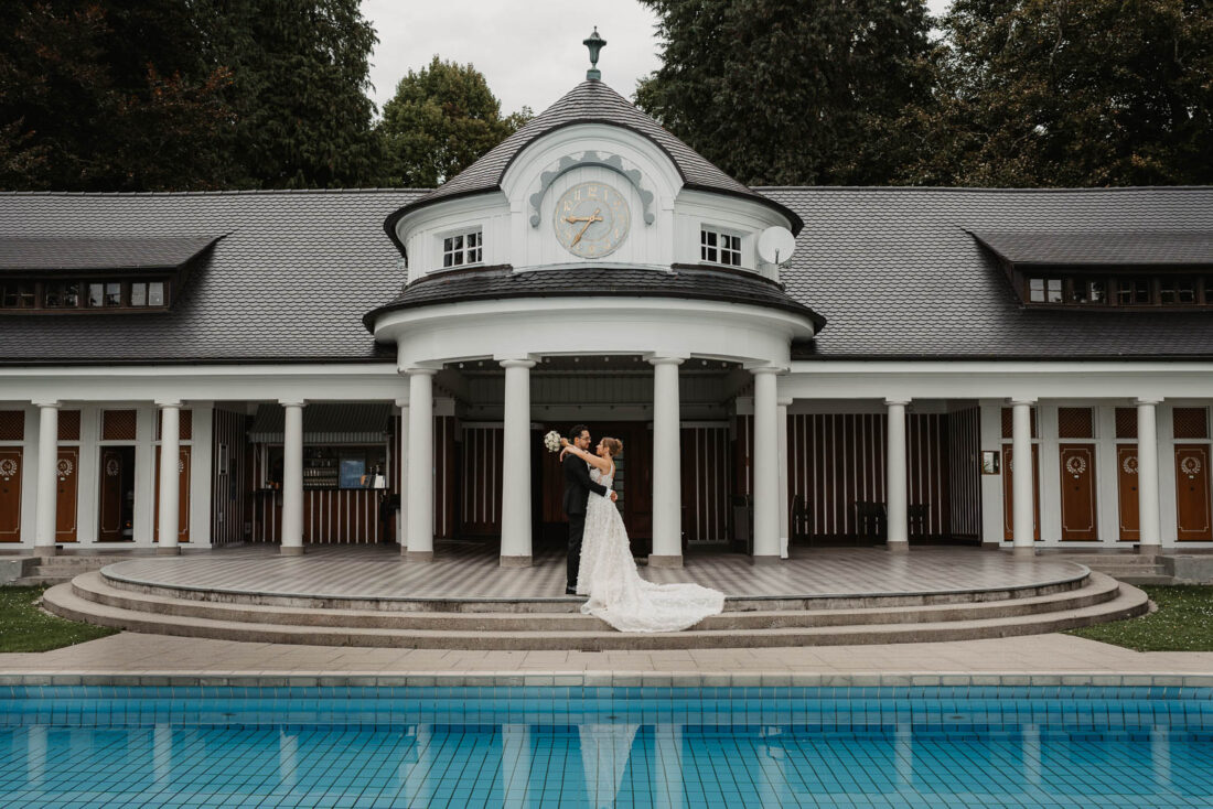 Das Paar umarmt sich vor dem markanten Rundbau des Strandbads in Lindau am Pool.
