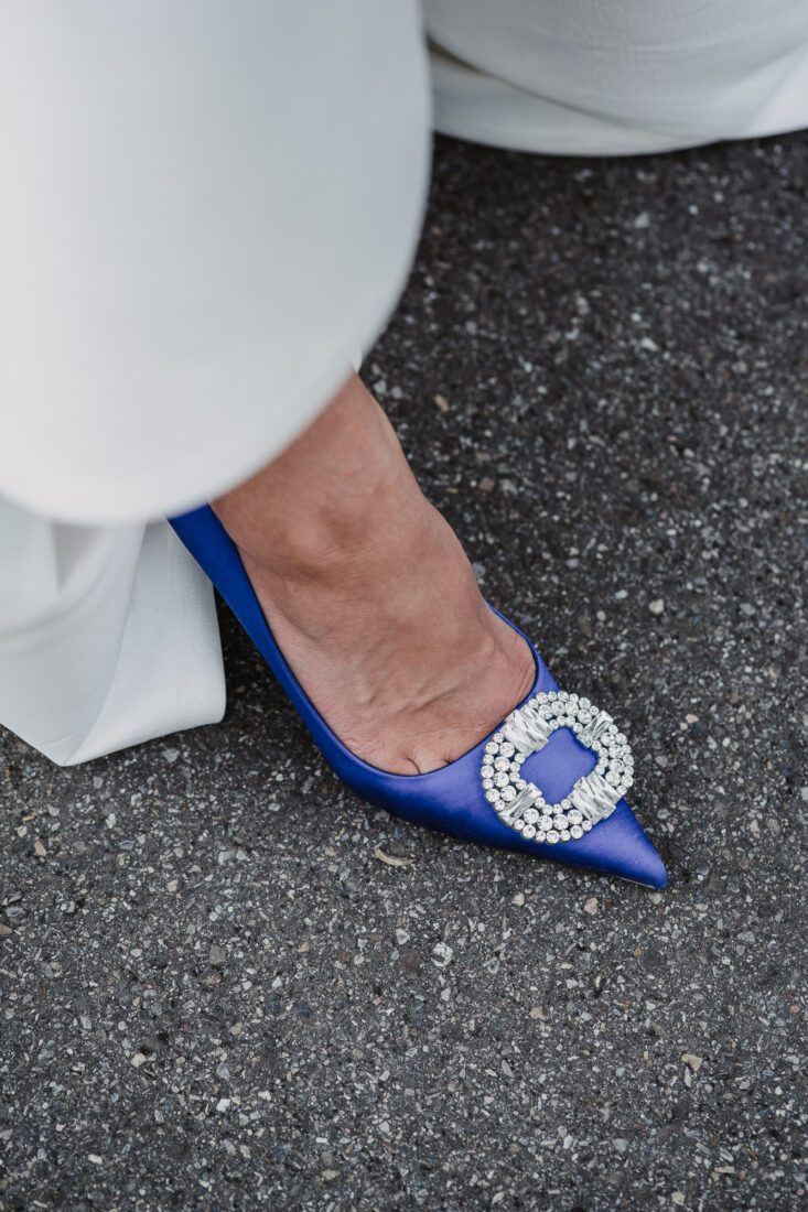 Nahaufnahme eines blauen Satin-Hochzeitsschuhs mit funkelnder Kristall-Schnalle auf Asphalt.