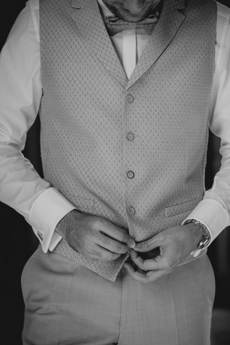 Detailaufnahme der Hände des Bräutigams beim Schließen der Weste