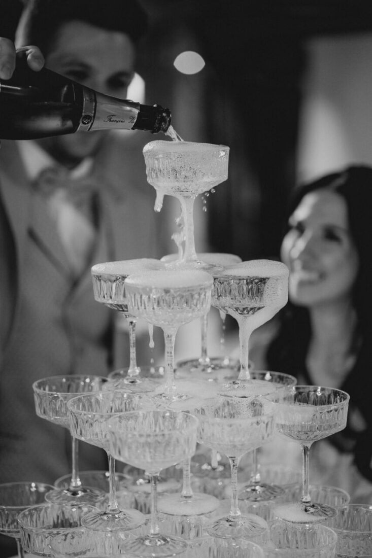 Nahaufnahme wie der Bräutigam den Champagner in die obersten Kristallgläser der Pyramide einschenkt.