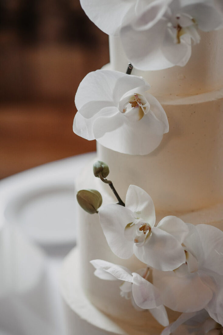 Nahaufnahme der zarten Orchideen-Blüten an einer minimalistischen weißen Hochzeitstorte.