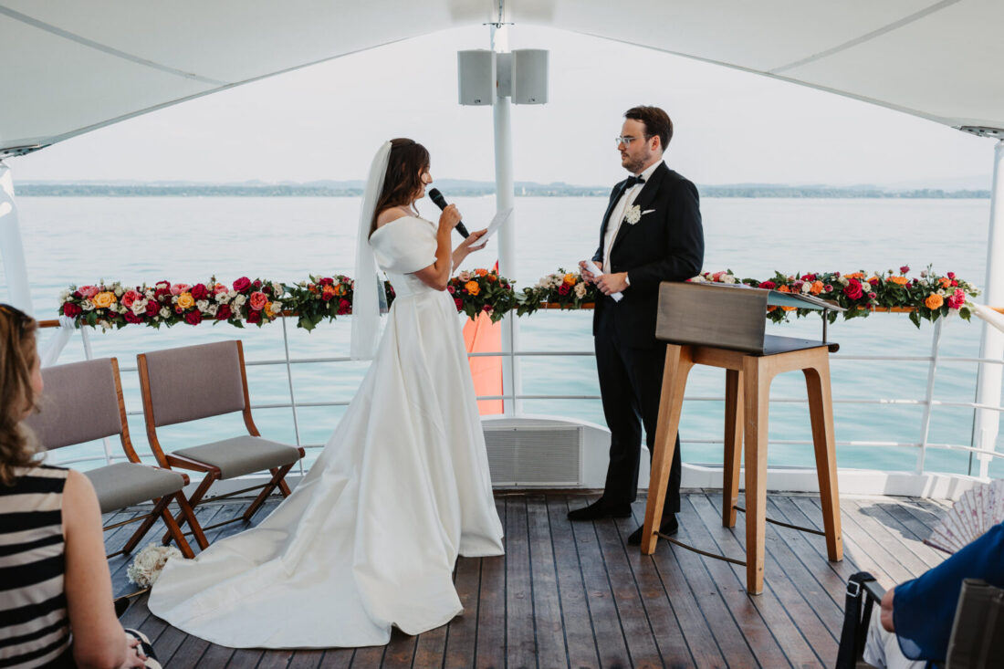 Die Braut liest ihr Eheversprechen in ein Mikrofon, während der Bräutigam sie gerührt auf dem Deck der MS Säntis ansieht.