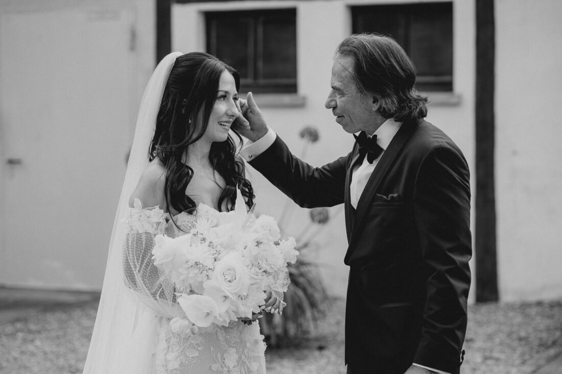 Nahaufnahme in Schwarz-Weiß: Der Vater wischt der Braut während eines emotionalen Moments auf dem Steinbachhof eine Träne aus dem Gesicht.