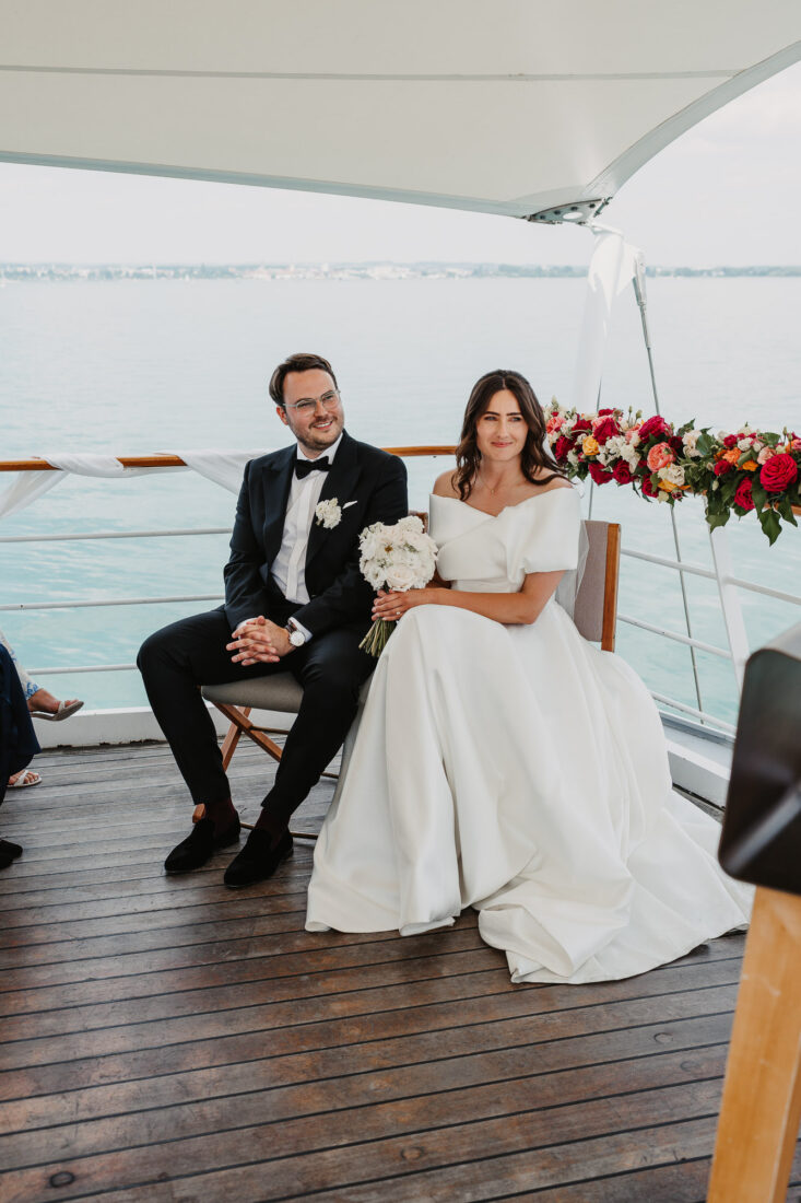 Braut und Bräutigam sitzen lächelnd auf dem Außendeck der MS Säntis während ihrer freien Trauung auf dem Wasser.