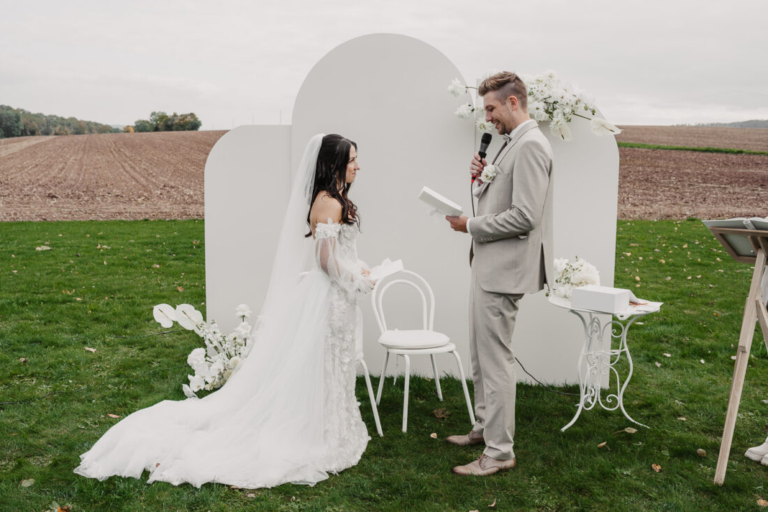 Brautpaar gibt sich das Eheversprechen vor einer modernen weißen Backdrop-Kulisse auf dem Steinbachhof.
