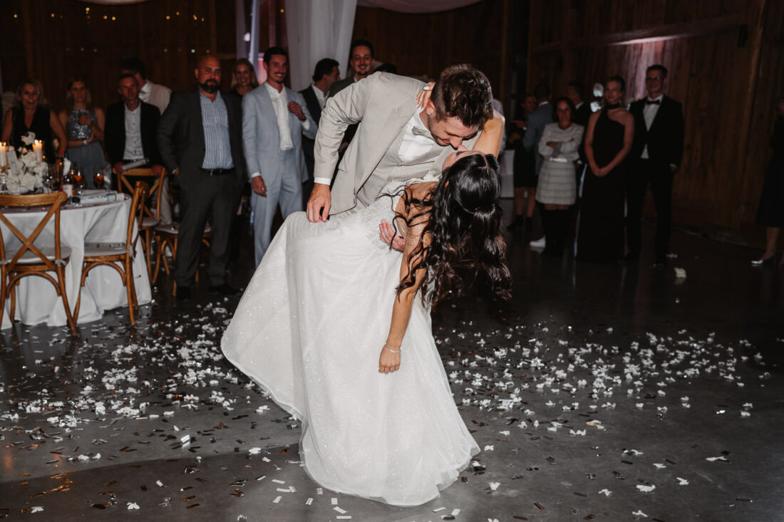 Braut und Bräutigam küssen sich beim ausgelassenen Tanz auf der Hochzeitsfeier im Kreise ihrer Gäste.