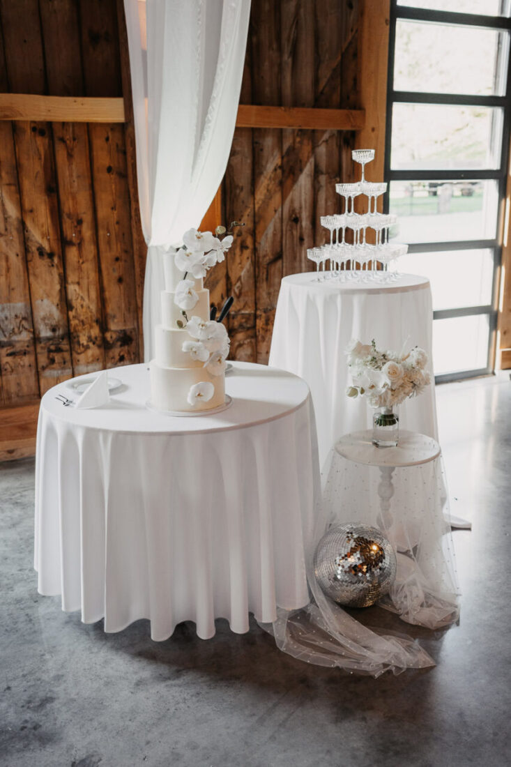 Elegantes Hochzeits-Setup auf dem Steinbachhof mit weißer Orchideen-Torte, Champagnerpyramide und Discokugel.