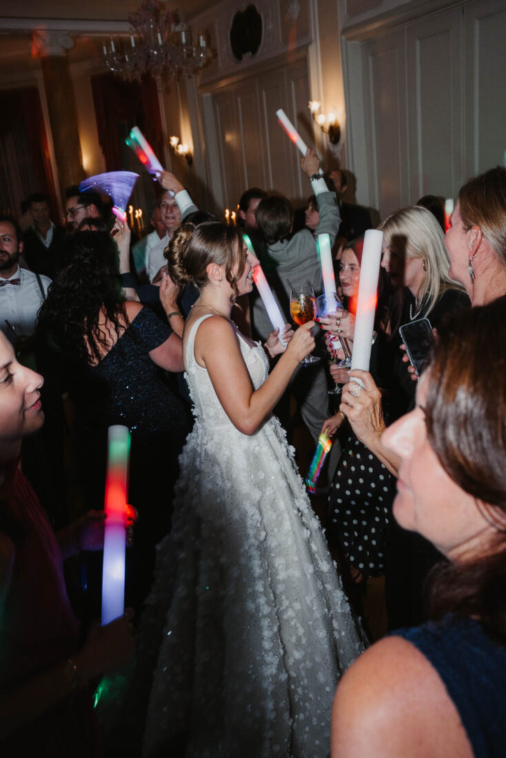 Die Braut tanzt ausgelassen mit bunten Leuchtstäben inmitten ihrer Gäste auf der Tanzfläche im Hotel Bad Schachen.