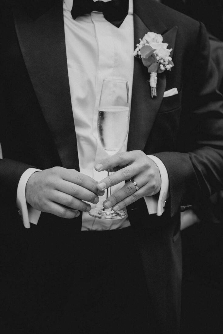 Detailaufnahme eines Bräutigams im Smoking mit Sektglas und Ehering bei der Hochzeit im Hotel Bad Schachen.