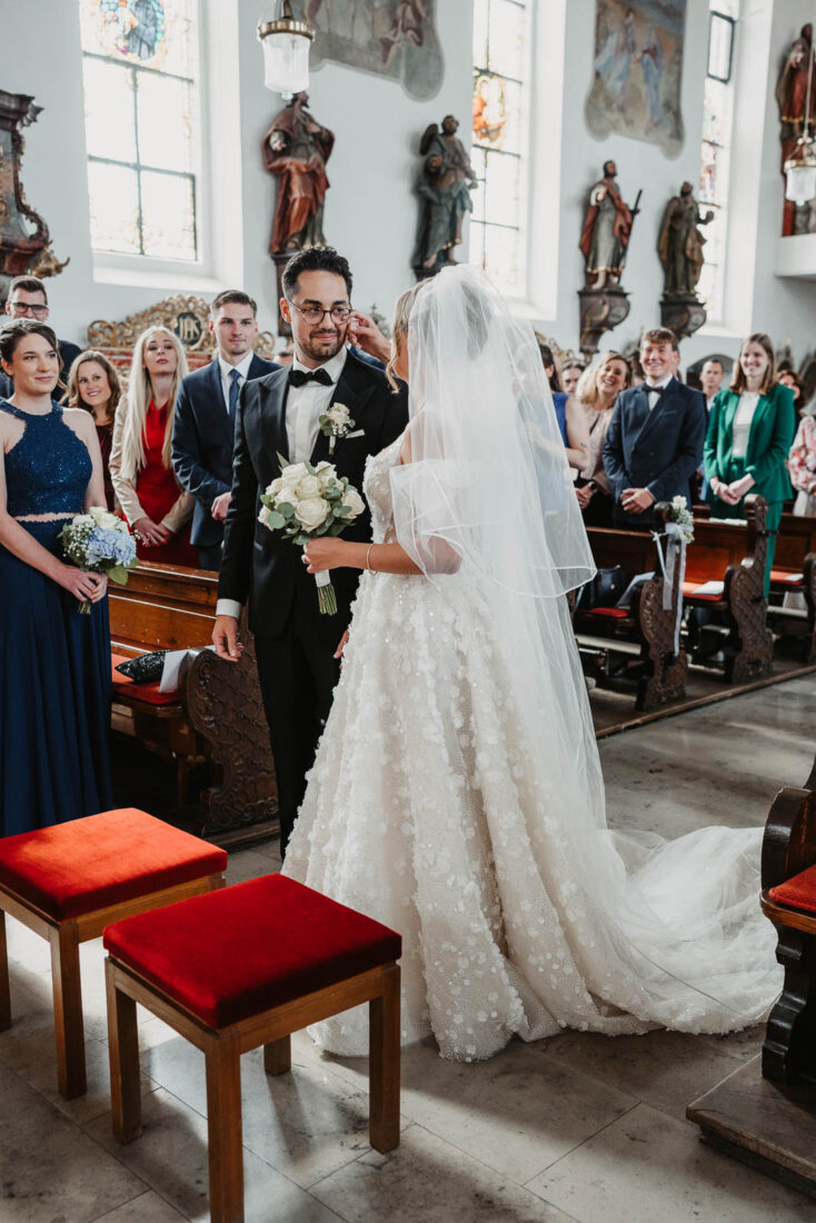 Die Braut wischt dem Bräutigam während der Zeremonie in einer Kirche in Lindau eine Träne ab.