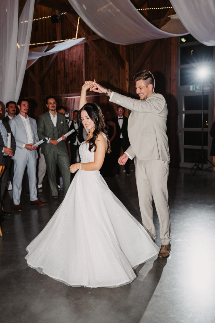 Der Bräutigam hält die Hand seiner Braut beim Eröffnungstanz in der Festscheune die mit weißen Leinen dekoriert wurde.