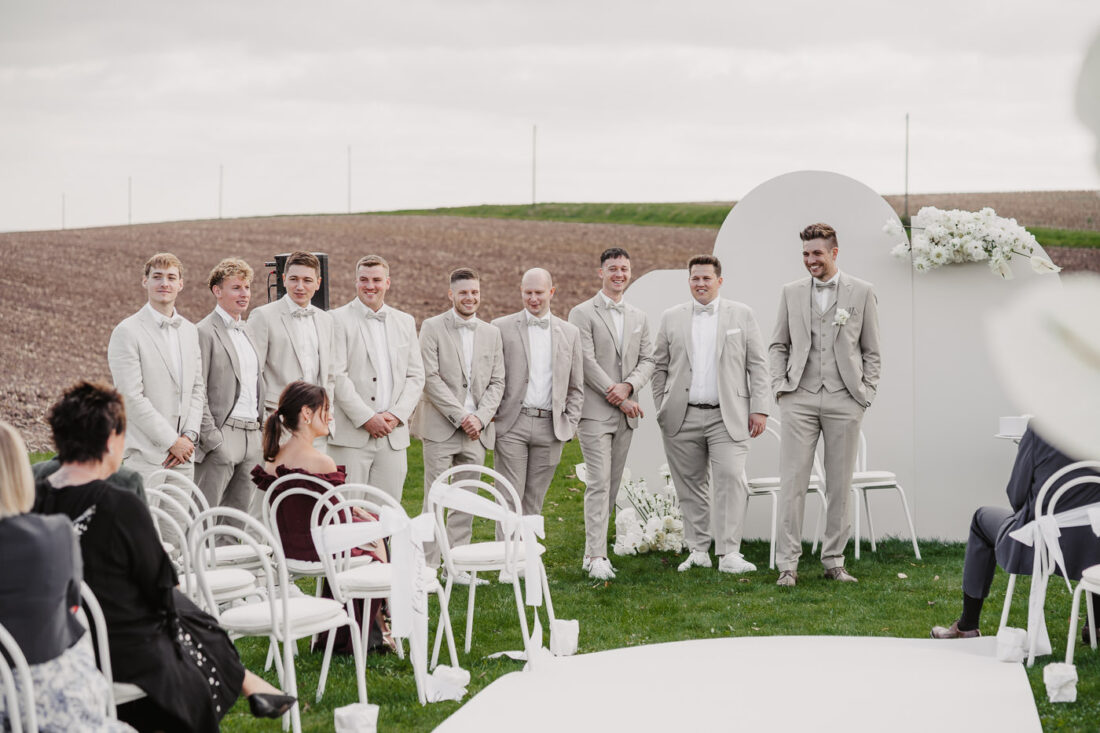Der Bräutigam steht mit seinen Trauzeugen und Groomsmen in hellen Anzügen vor der modernen Traukulisse auf dem Steinbachhof.