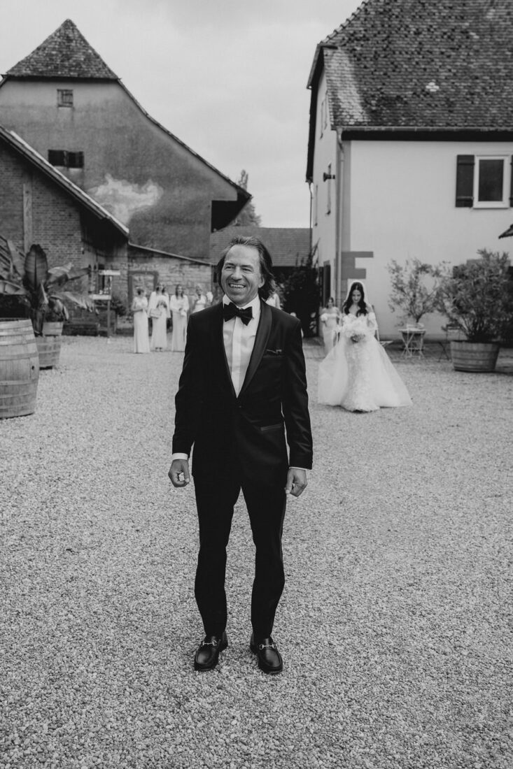 Braut im eleganten Hochzeitskleid mit langem Schleier tritt auf ihren Vater zu, der sie auf dem Steinbachhof zum ersten Mal sieht.