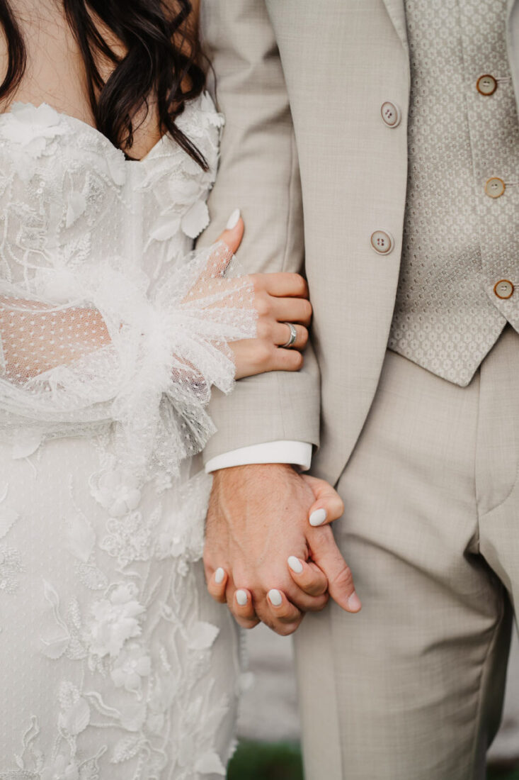 Detailaufnahme wie Braut und Bräutigam sich an den Händen halten und ihre Eheringe zeigen.