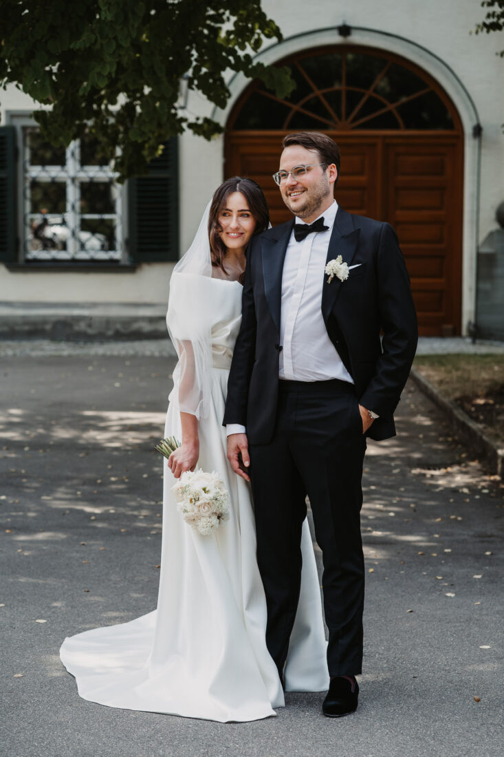 Ganzkörperaufnahme des Brautpaares unter einem Baumschatten vor dem Schloss in Friedrichshafen