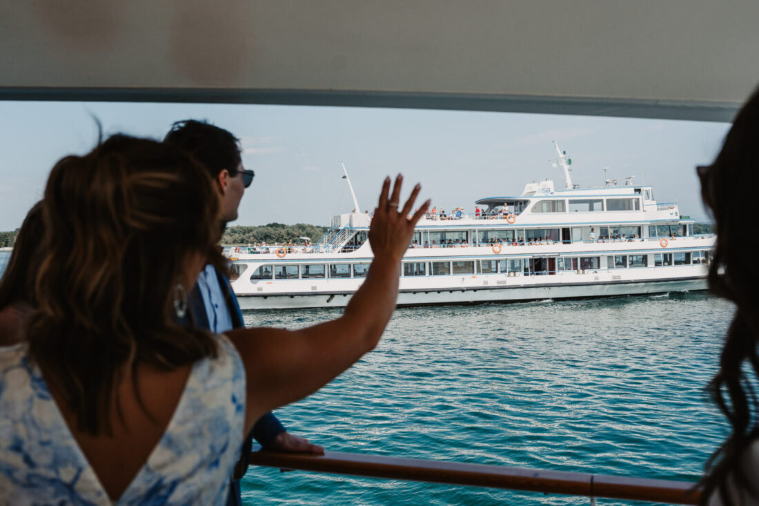 Hochzeitsgast auf der MS Säntis winkt einem vorbeifahrenden Schiff auf dem Bodensee zu.