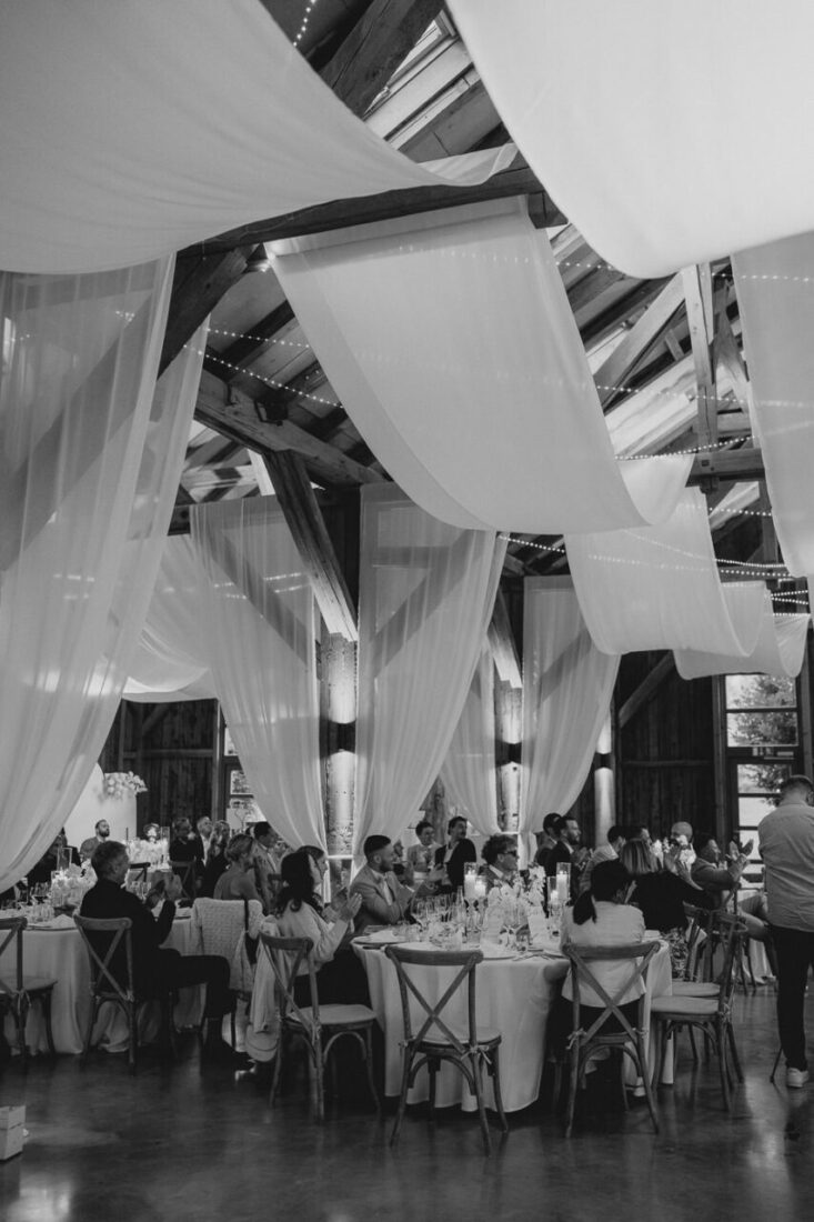 Blick in die festlich geschmückte Scheune des Steinbachhofs mit hängenden weißen Stoffen und Gästen an runden Tischen.