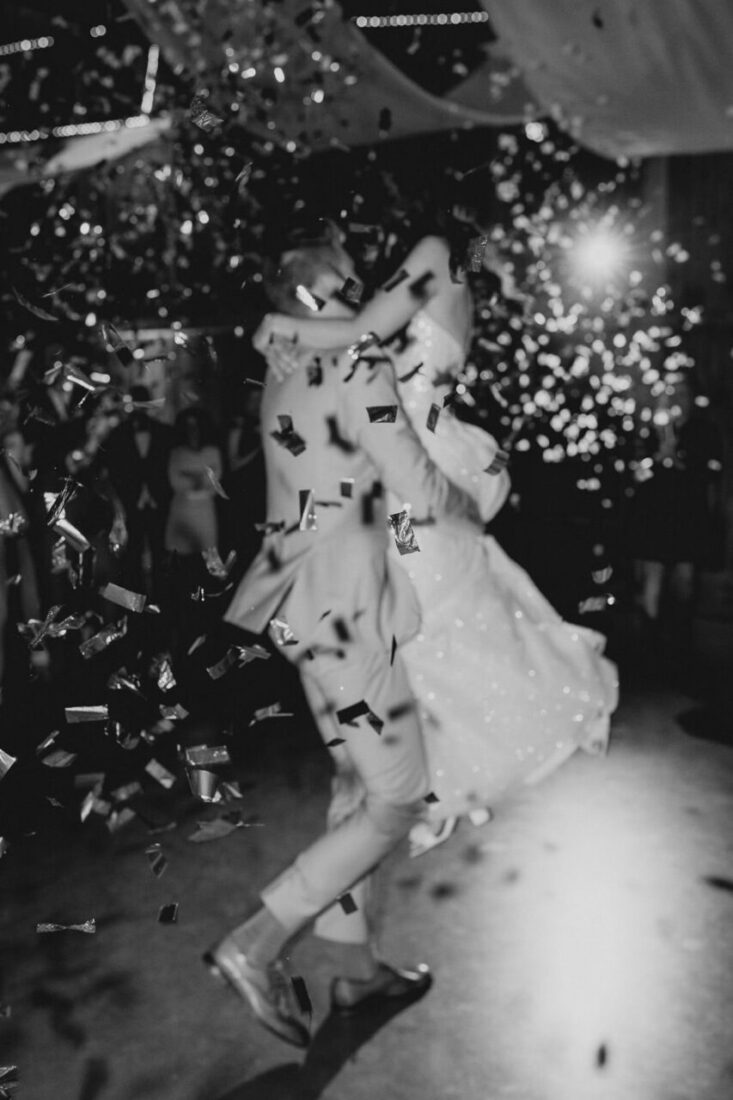 Dynamische Schwarz-Weiß-Aufnahme des Brautpaares inmitten eines glitzernden Konfetti-Regens auf der Tanzfläche.