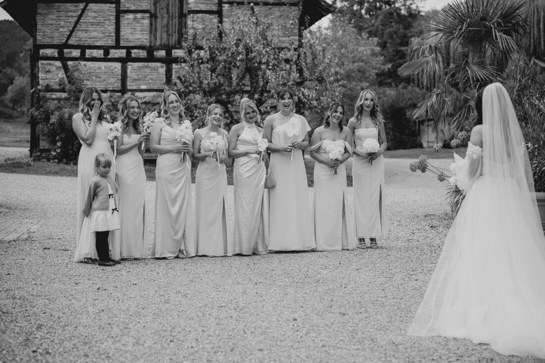 Brautjungfern reagieren mit offenem Mund und Begeisterung auf die Braut (Schwarz-Weiß).