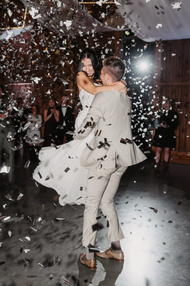 Bräutigam hebt Braut beim Eröffnungstanz unter Konfettiregen in die Höhe.