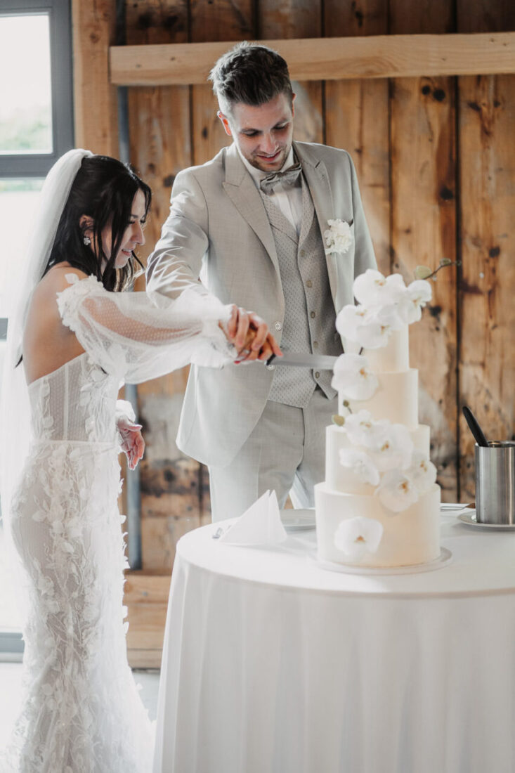 Das Brautpaar schneidet die vierstöckige Hochzeitstorte mit Orchideen-Verzierung an.
