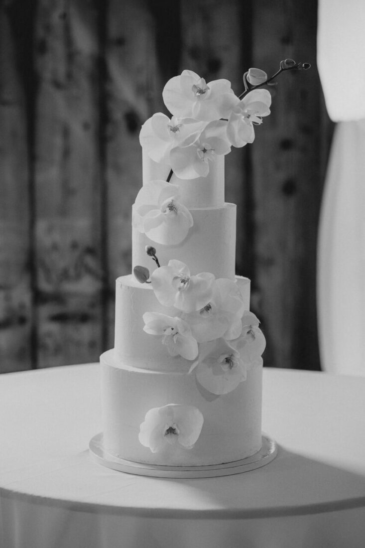 Zeitlose vierstöckige Hochzeitstorte mit Orchideen-Verzierung in einer Schwarz-Weiß-Aufnahme.