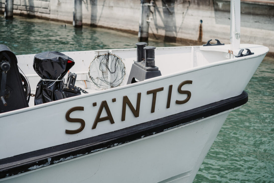 Detailansicht des Schriftzugs "Säntis" am Bug des Schiffes auf dem klaren Wasser des Bodensees.