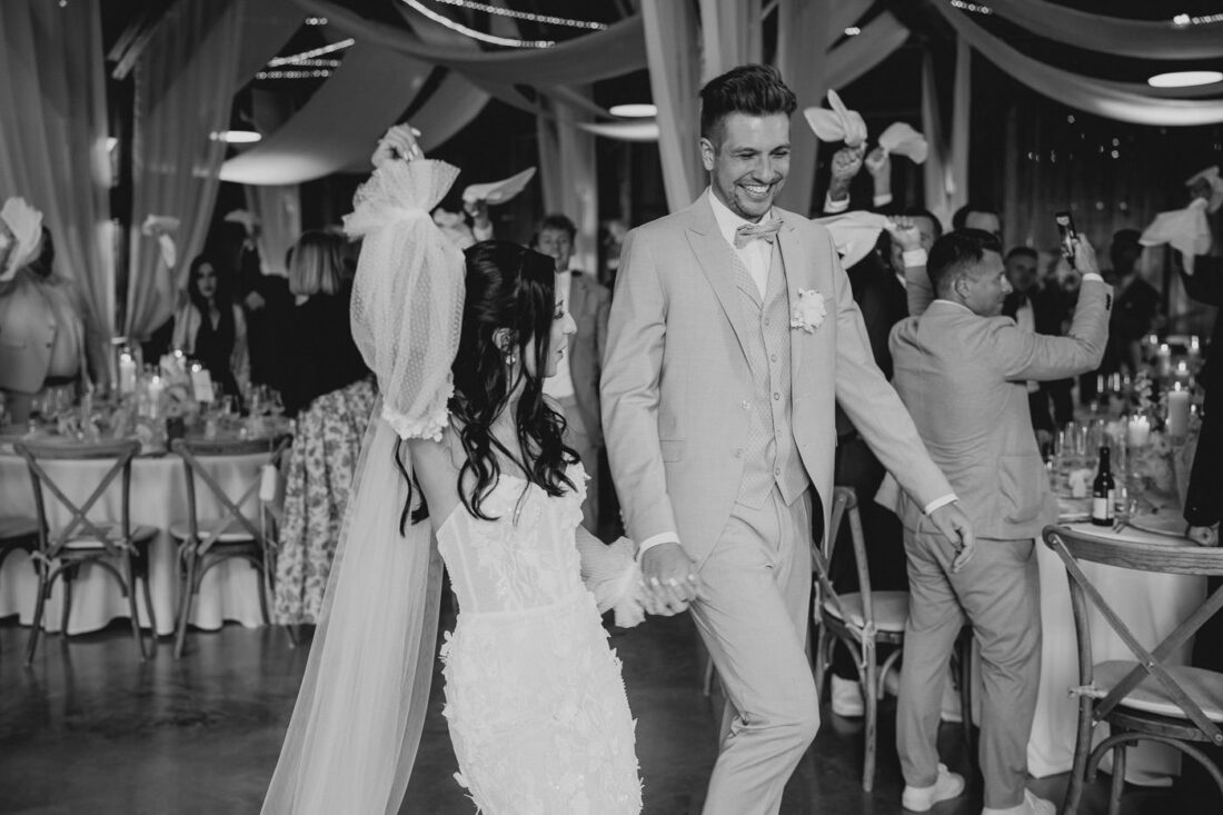 Das Brautpaar genießt den Moment des Einzugs in die Festscheune und jubelt mit den Händen nach oben.